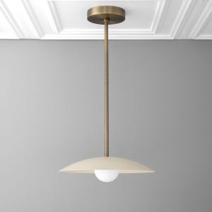 May include: A brass pendant light with a white, saucer-shaped shade and a round, white light bulb.
