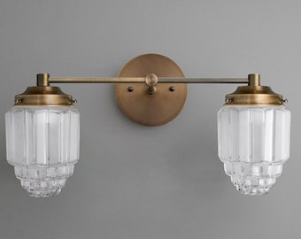 May include: A brass double-arm wall sconce with two frosted glass shades. The shades have a geometric, layered design.