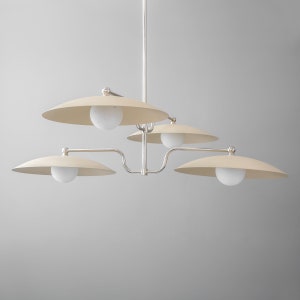 May include: A modern chrome and cream chandelier with five lights. The chandelier has a central stem with four arms extending out, each with a cream-colored shade and a white globe light bulb.