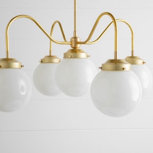 May include: A brass chandelier with five white globe-shaped glass shades. The chandelier has a curved, modern design.