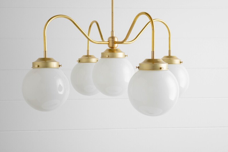May include: A brass chandelier with five white globe-shaped glass shades. The chandelier has a curved, modern design.