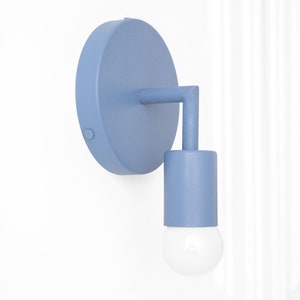 Puede incluir: Una l&aacute;mpara de pared de color azul claro con una placa trasera redonda y una pantalla cil&iacute;ndrica. La l&aacute;mpara tiene un dise&ntilde;o simple y moderno.