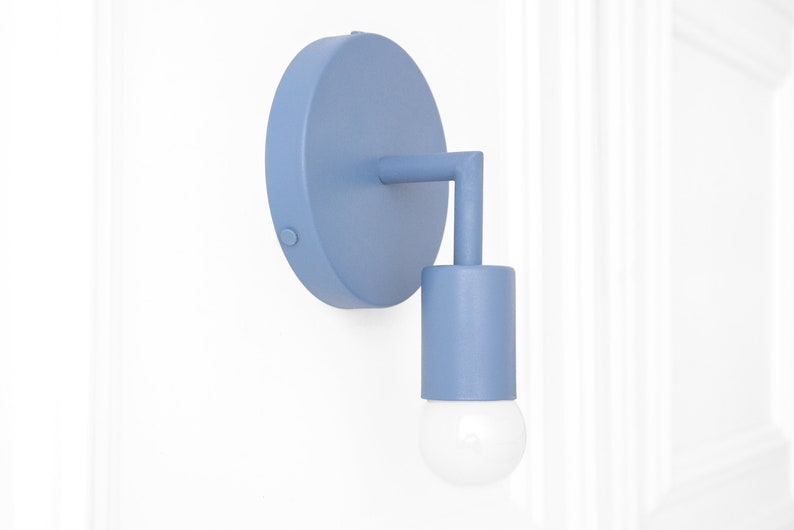 Puede incluir: Una l&aacute;mpara de pared de color azul claro con una placa trasera redonda y una pantalla cil&iacute;ndrica. La l&aacute;mpara tiene un dise&ntilde;o simple y moderno.