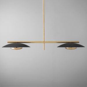 May include: A modern brass and black pendant light fixture with two shades. The fixture has a long, horizontal bar with two shades that hang down from it.