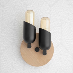 May include: A pair of black wall sconces with round wooden bases and clear glass bulbs. The sconces are mounted on a white wall with a geometric pattern.