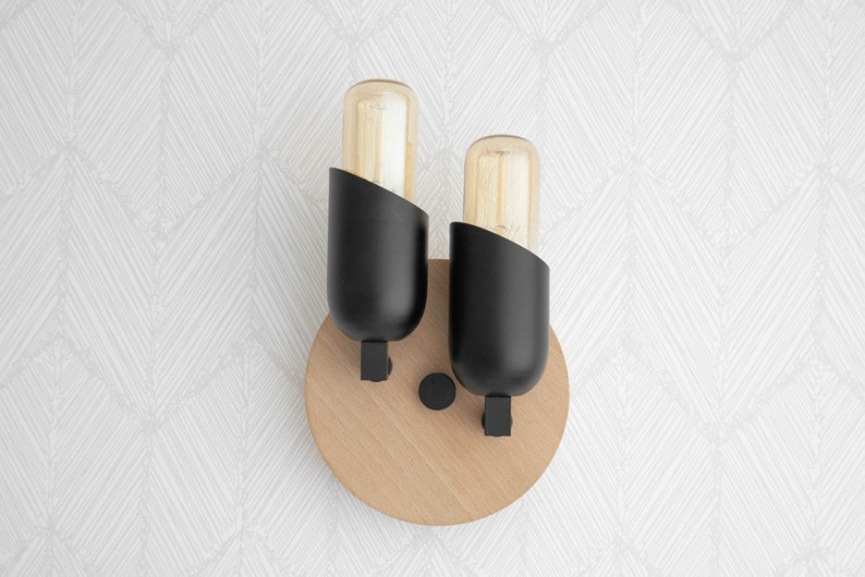 May include: A pair of black wall sconces with round wooden bases and clear glass bulbs. The sconces are mounted on a white wall with a geometric pattern.