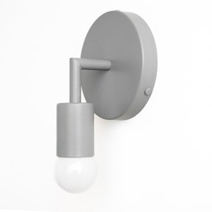 Puede incluir: Una l&aacute;mpara de pared plateada con una placa trasera redonda y una luminaria cil&iacute;ndrica. La luminaria tiene una bombilla de vidrio transparente.