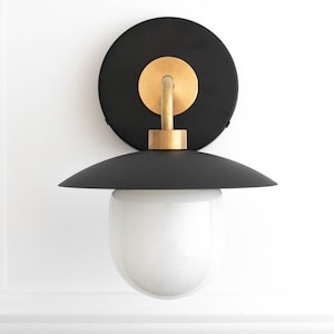 May include: A black and gold wall sconce with a white glass globe shade. The sconce has a round back plate and a curved arm.