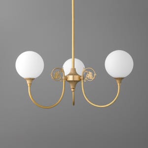 May include: A gold three-light chandelier with white globe-shaped shades. The chandelier has a decorative design with ornate details.