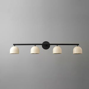 May include: A modern, four-light vanity fixture. The light features a black metal bar and circular wall mount. Four cream-colored, dome-shaped shades are evenly spaced along the bar. The fixture is designed for bathroom or vanity use.
