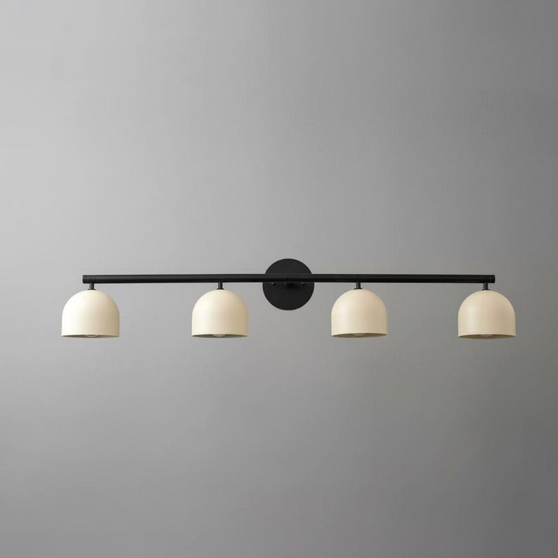 May include: A modern, four-light vanity fixture. The light features a black metal bar and circular wall mount. Four cream-colored, dome-shaped shades are evenly spaced along the bar. The fixture is designed for bathroom or vanity use.