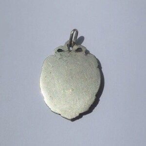 K&ouml;nnte beinhalten: Ein silberfarbener Metallanh&auml;nger in Schildform mit einer glatten, flachen Oberfl&auml;che und einem dekorativen, gewellten Rand. Der Anh&auml;nger verf&uuml;gt &uuml;ber eine kleine, integrierte Metall&ouml;se an der Oberseite zur Befestigung und weist ein gleichm&auml;&szlig;iges Metallfinish auf.