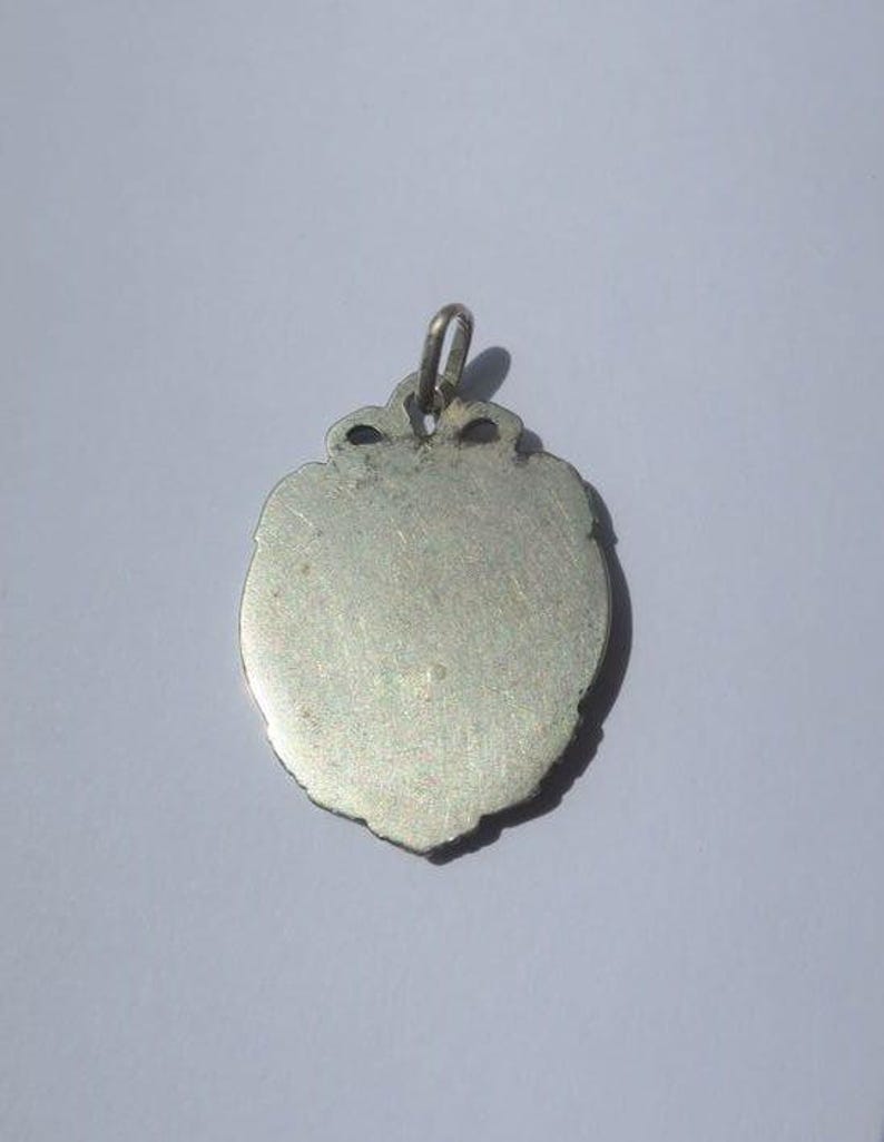 K&ouml;nnte beinhalten: Ein silberfarbener Metallanh&auml;nger in Schildform mit einer glatten, flachen Oberfl&auml;che und einem dekorativen, gewellten Rand. Der Anh&auml;nger verf&uuml;gt &uuml;ber eine kleine, integrierte Metall&ouml;se an der Oberseite zur Befestigung und weist ein gleichm&auml;&szlig;iges Metallfinish auf.