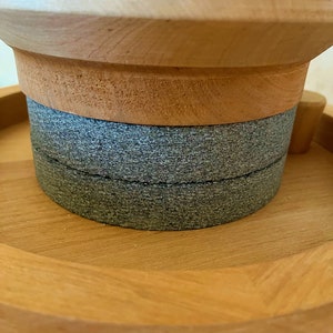 May include: Close-up of a wooden spice grinder with a gray stone grinding wheel. The grinder is made of light wood and has a round shape.