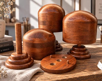 May include: A set of three polished wooden hat blocks with a rich brown grain, featuring two dome-shaped forms on tiered circular bases and one tall cylindrical post. A flat circular wooden base with three holes and two small pegs is included.