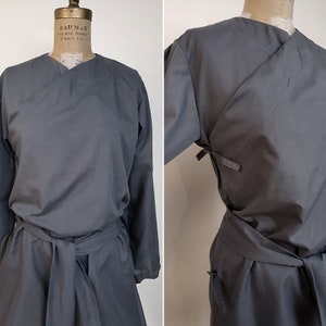 May include: A gray wrap dress with long sleeves and a tie belt. The dress has a V-neckline and a simple design.