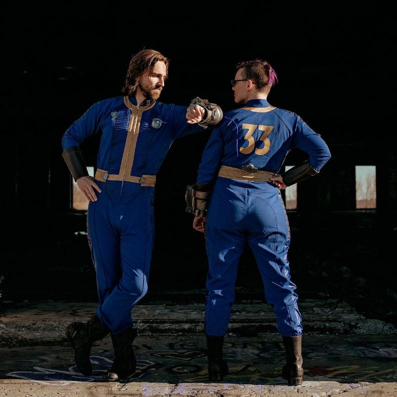 May include: Two blue jumpsuits featuring gold trim, a central zipper, and a gold number 33 on the back. The jumpsuits include black forearm guards, a gold belt, and dark boots. One jumpsuit displays a small emblem on the chest and ribbed detailing.