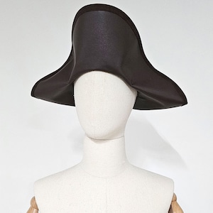 May include: A brown felt tricorn hat with a wide brim. The hat is on a white mannequin head.