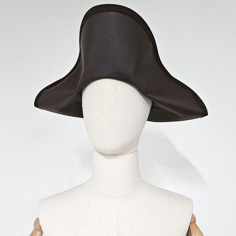 May include: A brown felt tricorn hat with a wide brim. The hat is on a white mannequin head.