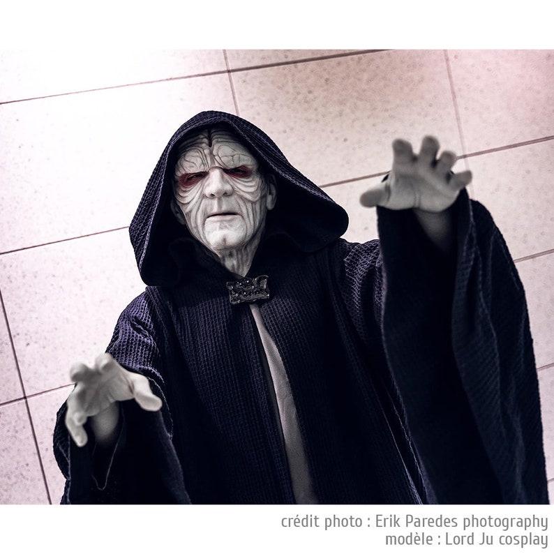 May include: A person dressed as Darth Sidious from Star Wars, wearing a black hooded robe with a white undergarment. The character has a pale face with red eyes and a dark expression.