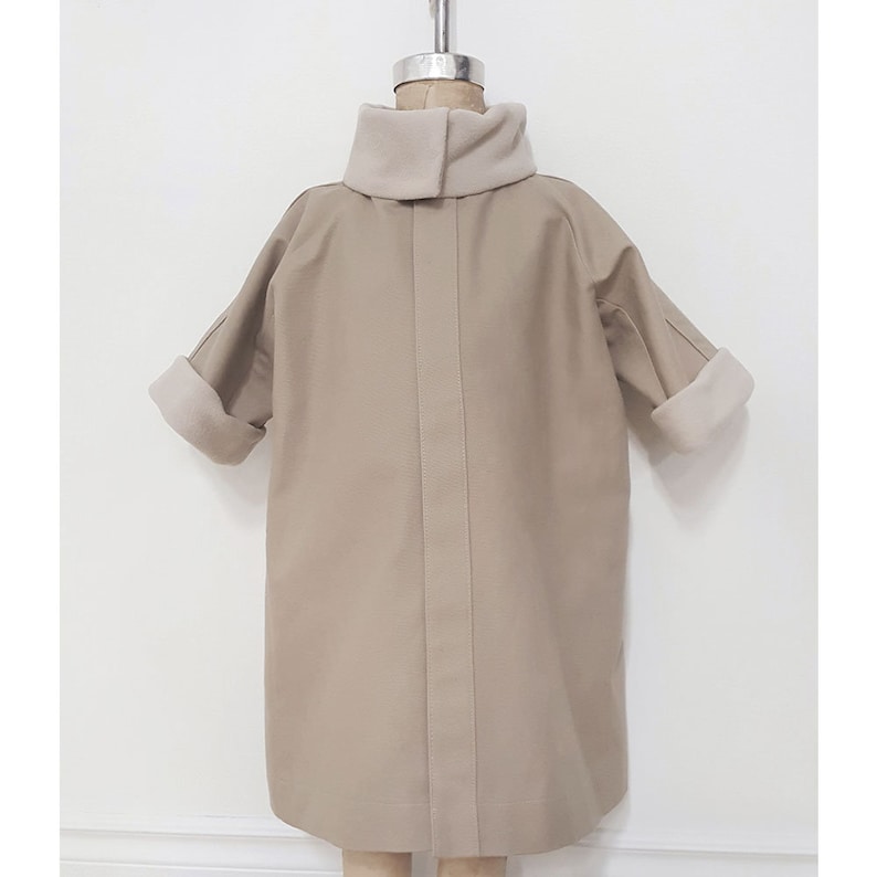 Puede incluir: Un abrigo beige de manga larga con cuello alto y forro de borreguito blanco en el cuello y los pu&ntilde;os.