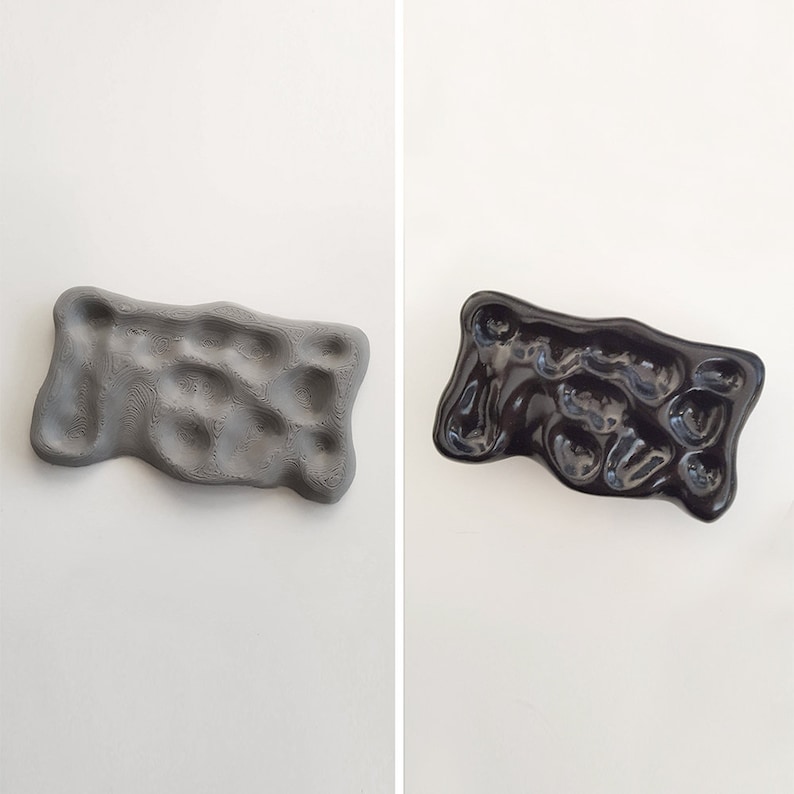 May include: Two ceramic trays, one gray and one black, with a textured, organic, and slightly bumpy surface. The trays have a unique, abstract shape.