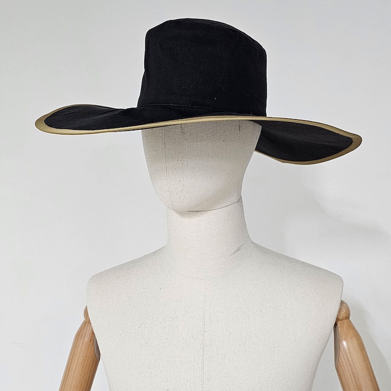 May include: A wide-brimmed black hat with a tan trim. The hat is sitting on a white mannequin head.