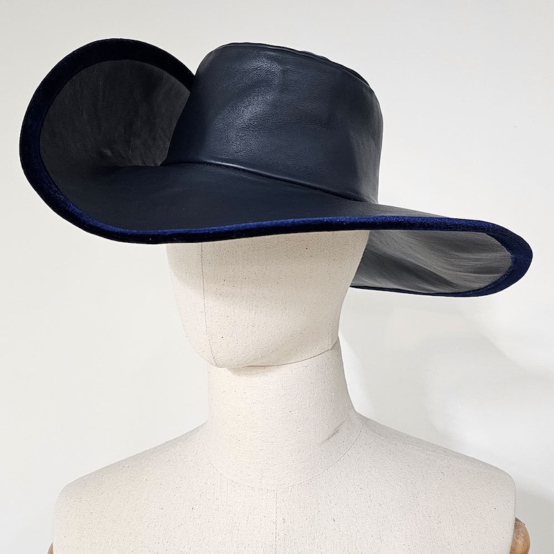 May include: A wide-brimmed hat with a navy blue leather crown and brim. The brim has a dark blue velvet trim.