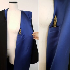 May include: A black coat with a royal blue satin lining and a gold pocket square. The coat is displayed on a mannequin, showcasing the contrast between the dark exterior and the vibrant interior. The pocket square adds a touch of elegance.