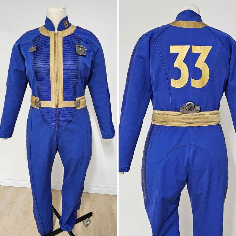 May include: A blue jumpsuit featuring gold accents, a front zipper, and the number 33 displayed on the back. The garment includes pleated panels on the chest, a gold belt, and a small mechanical-style device attached to the back of the waistband.