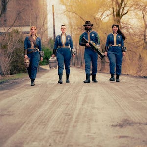 May include: Four individuals wearing blue jumpsuits with yellow trim and circular patches on the chest. They are equipped with various accessories including brown leather straps, dark wrist guards, a metallic box, and a large prop rifle.