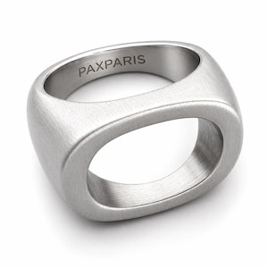 Op de afbeelding: Een geborstelde zilveren ring met een rechthoekig ontwerp en afgeronde randen. De ring heeft een ovale opening in het midden. Het woord "PAXPARIS" is gegraveerd op de bovenkant van de ring.