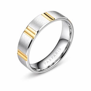 Puede incluir: Un anillo plateado con dos franjas doradas. El anillo tiene un acabado cepillado en la parte superior y un interior pulido. El texto "PAXPARIS" está grabado en el interior. Una joya.