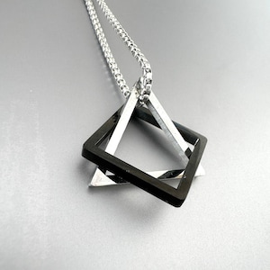 May include: A silver chain necklace with a pendant featuring two overlapping square geometric shapes. One square is black, and the other is silver. The pendant hangs from a silver chain.