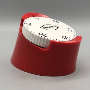 May include: A red kitchen timer with a white circular dial featuring black numbers from zero to fifty and the brand name MIRRO printed in the center. The timer has a ridged white edge and is set within a solid red, slightly angled plastic base.