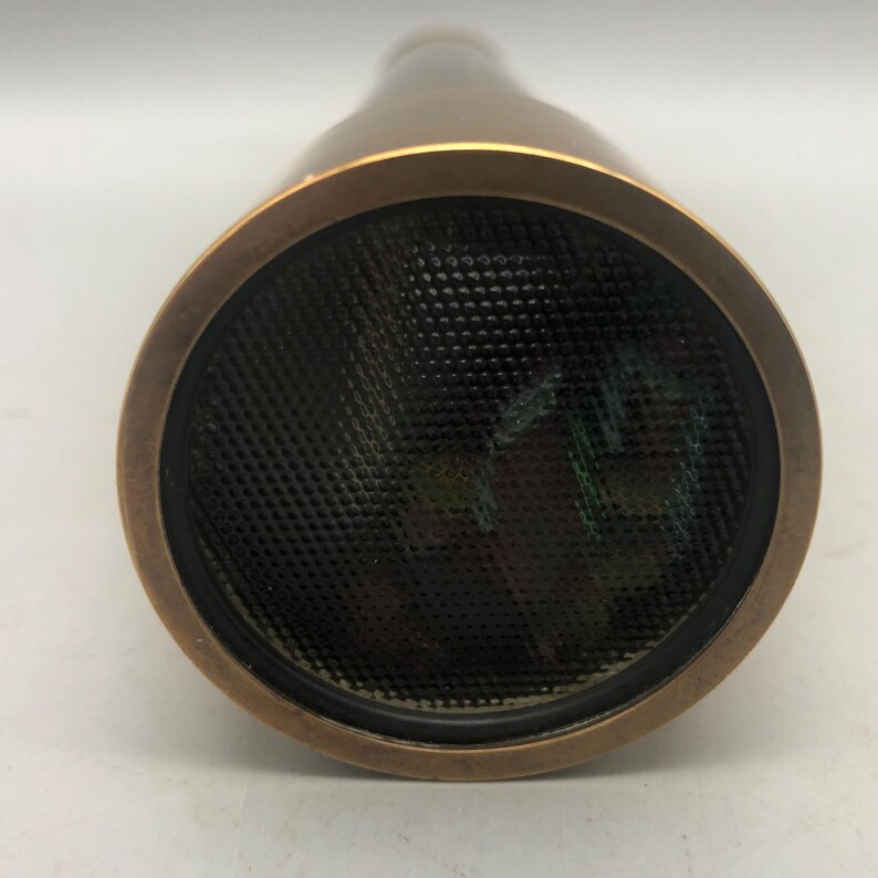 May include: A bronze kaleidoscope with a black mesh lens. The kaleidoscope has a circular lens and a cylindrical body. The lens is surrounded by a bronze ring. The body of the kaleidoscope is bronze in colour.