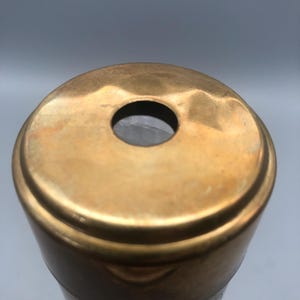 May include: Close-up of a brass kaleidoscope with a circular viewing hole. The brass has a warm, golden hue and shows signs of age. The body of the kaleidoscope is cylindrical, with a darker band near the base.