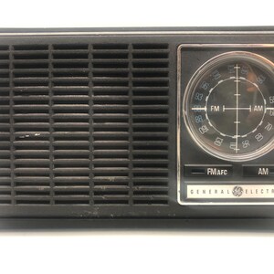 May include: A black vintage General Electric AM/FM radio with a silver face and a round dial with numbers and markings for FM and AM frequencies. The radio has a speaker grille on the left side and buttons for FM/AFC and AM.