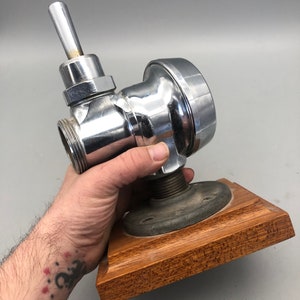 May include: A chrome-plated plumbing valve with a lever handle, mounted on a wooden base.