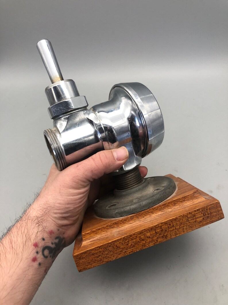 May include: A chrome-plated plumbing valve with a lever handle, mounted on a wooden base.