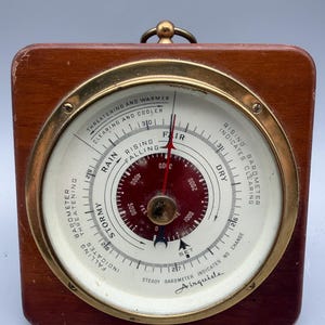 May include: A vintage Airguide barometer with a wooden frame and a brass bezel. The circular gauge features a white face with black and red markings, indicating weather conditions. The barometer measures altitude in feet.