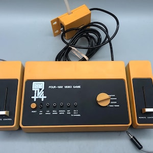 May include: Vintage orange and black Four-Way Video Game console with two remote controls and a separate antenna. The console features buttons for game selection and channel control. The text "FOUR-WAY VIDEO GAME" is printed on the front.