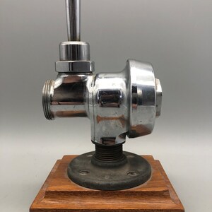 May include: A chrome-plated faucet with a wooden base. The faucet has a lever handle and a round body. The base is made of dark wood.