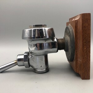 May include: A chrome-plated toilet cistern fill valve with a wooden mounting plate. The valve has a lever handle and a threaded connection.