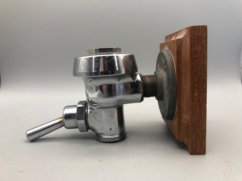 May include: A chrome-plated toilet cistern fill valve with a wooden mounting plate. The valve has a lever handle and a threaded connection.