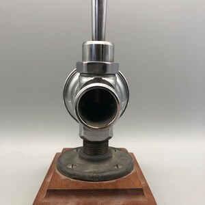 May include: A chrome faucet with a lever handle mounted on a wooden base. The faucet has a round body and a cylindrical spout.