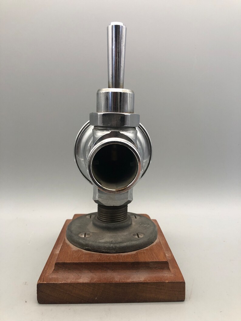 May include: A chrome faucet with a lever handle mounted on a wooden base. The faucet has a round body and a cylindrical spout.