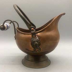 May include: A copper ice bucket with a handle and a porcelain knob. The bucket has a decorative lion head design on the side.
