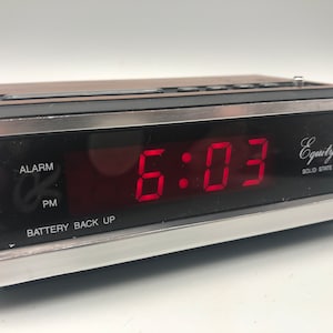 May include: A vintage red digital clock with a black and silver case. The clock displays the time 5:03 PM and has an alarm function. The clock is labeled "Equity Solid State".