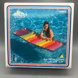 May include: A rainbow-colored inflatable pool float with a person sitting on it in a swimming pool. The float is 74 inches long and 28 inches wide. The box has the text "The Wet Set" and "INTEX" on it.